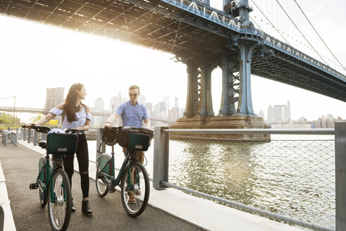 Paar, das mit Fahrrädern auf der Promenade am East River gegen die Manhattan-Brücke läuft - CAVF45358
