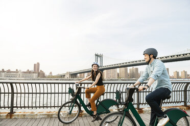 Glückliches Paar Radfahren auf dem Fußweg durch Manhattan Brücke gegen den Himmel - CAVF45370