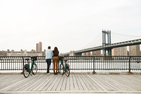 Paar steht mit Fahrrädern auf dem Fußweg bei der Manhattan-Brücke gegen den Himmel - CAVF45371