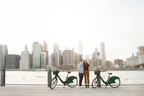 Paar, das ein Selfie macht, während es neben Fahrrädern am East River in der Stadt steht - CAVF45374