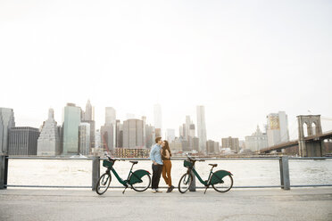 Paar, das sich umarmt, während es neben Fahrrädern am East River in der Stadt steht - CAVF45375