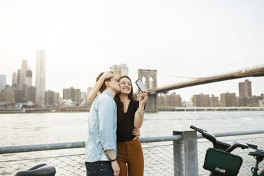 Man kissing happy woman photographing against East river in city - CAVF45376