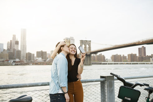 Mann küsst glückliche Frau beim Fotografieren gegen den East River in der Stadt - CAVF45376