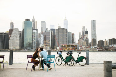 Couple kissing while sitting at sidewalk cafe by river in city - CAVF45377