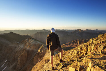 Rear view of man looking at mountains while standing on rock against clear sky - CAVF45442