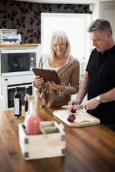 Ehepaar in der Küche, das ein digitales Tablet für ein Rezept verwendet und eine Mahlzeit zubereitet - MASF06587