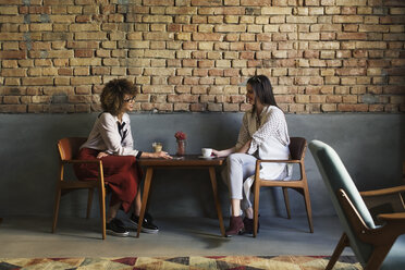 Lächelnde Geschäftsfrauen, die sich am Tisch in der Hotellobby unterhalten - CAVF45454