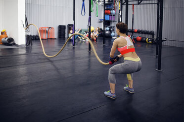 Rückansicht einer entschlossenen Sportlerin, die mit einem Seil im Fitnessstudio trainiert - CAVF45476