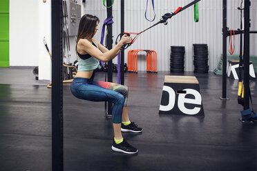 Seitenansicht einer entschlossenen Sportlerin beim Ziehen von Hängegurten im Fitnessstudio - CAVF45479