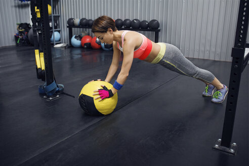 Weibliche Athletin in voller Länge, die sich im Fitnessstudio auf einen Medizinball stützt - CAVF45480