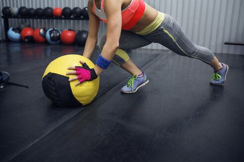 Tiefschnitt einer Sportlerin, die sich im Fitnessstudio auf einen Medizinball stützt - CAVF45481