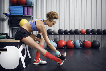 Seitenansicht einer Sportlerin, die im Sitzen auf einer Box im Fitnessstudio trainiert - CAVF45489
