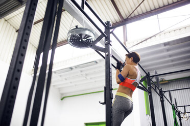 Low angle view of female athlete doing chin-ups at gym - CAVF45493