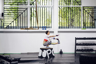 Seitenansicht eines weiblichen Sportlers, der in einem Fitnessstudio auf einer Box trainiert - CAVF45509