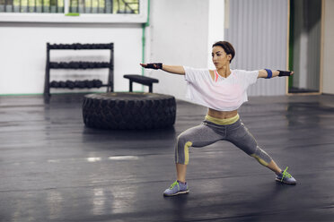 Entschlossener weiblicher Athlet, der im Fitnessstudio die Haltung des Kriegers 2 einnimmt - CAVF45510