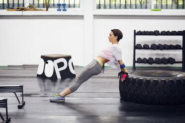 Seitenansicht eines weiblichen Athleten, der sich beim Training im Fitnessstudio auf einen Reifen stützt - CAVF45514