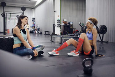 Happy female athletes talking while sitting on floor at gym - CAVF45523