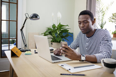 Young man using smart phone while working at home - CAVF45528