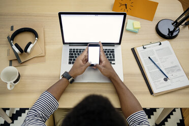 Draufsicht auf einen Mann, der im Büro zu Hause ein Smartphone und einen Laptop benutzt - CAVF45531