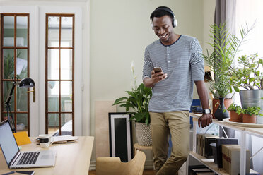 Happy man using smart phone at home office - CAVF45536