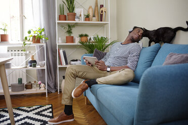 Man looking at cat while sitting on sofa in living room - CAVF45540