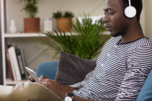 Seitenansicht eines Mannes, der einen Tablet-Computer benutzt, während er zu Hause auf dem Sofa sitzt - CAVF45542