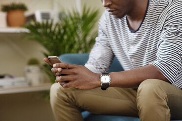 Midsection of man using smart phone while sitting on sofa at home - CAVF45544