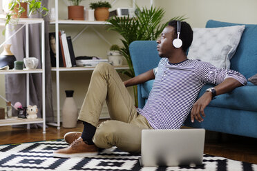 Thoughtful man listening music while sitting on floor in living room - CAVF45546