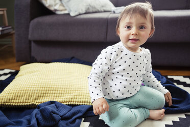 Portrait of cute baby girl sitting on rug in living room - CAVF45552