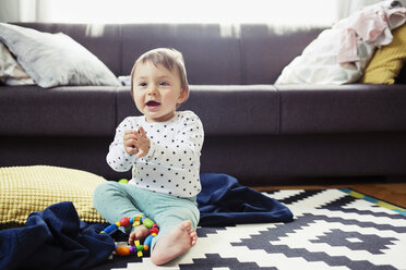 Glückliches kleines Mädchen sitzt auf dem Teppich im Wohnzimmer - CAVF45553