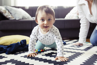 Porträt eines glücklichen kleinen Mädchens, das mit seiner Großmutter im Wohnzimmer auf dem Teppich krabbelt - CAVF45554