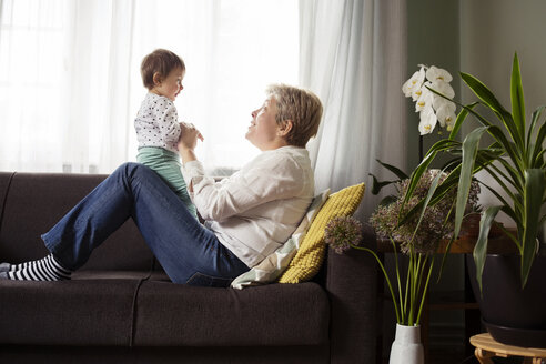 Seitenansicht einer glücklichen Frau, die mit ihrer Enkelin auf dem Sofa am Fenster spielt - CAVF45560
