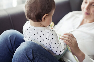 Grandmother sitting with granddaughter on sofa at home - CAVF45565