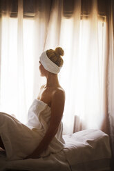 Side view of thoughtful woman sitting on massage table in spa - CAVF45574