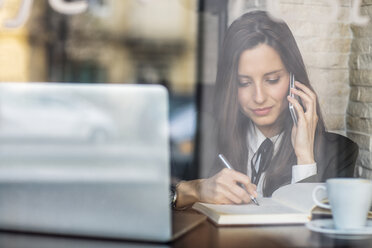 Geschäftsfrau, die ein Smartphone benutzt, während sie in einem Café in ihr Tagebuch schreibt - CAVF45613