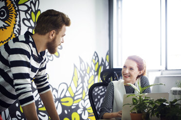 Happy businesswoman discussing with male colleague in creative office - CAVF45636