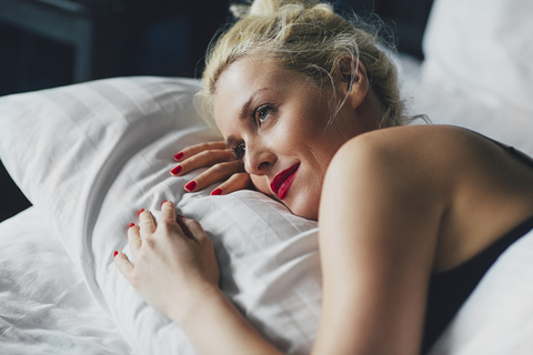 Nahaufnahme einer nachdenklichen Frau, die sich auf dem Bett entspannt, lizenzfreies Stockfoto