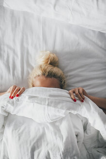 Draufsicht auf eine Frau, die ihr Gesicht mit einer Decke auf dem Bett bedeckt - CAVF45662