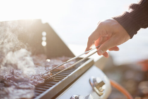 Nahaufnahme eines Mannes, der Rindfleisch mit einer Zange auf dem Grill wendet - MASF06595