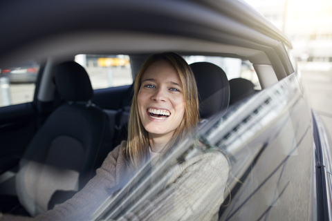 Porträt einer lachenden jungen Frau, die im Auto sitzt, lizenzfreies Stockfoto