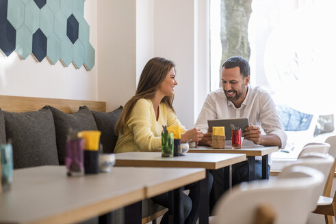 Junge Frau und glücklicher Mann mit Tablet in einem Cafe - DIGF03922