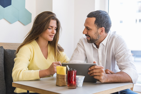 Junge Frau und Mann teilen sich ein Tablet in einem Cafe, lizenzfreies Stockfoto