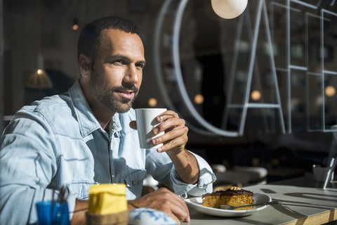 Smiling man drinking coffee and eating cake in a cafe stock photo