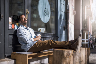Entspannter Mann sitzt vor einem Café und genießt die Sonne - DIGF03952