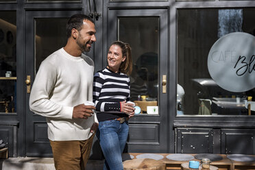 Mann und Frau mit Bechern zum Mitnehmen gehen vor einem Cafe - DIGF03954