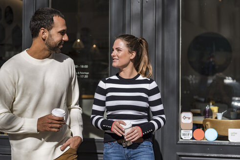 Mann und Frau halten Tassen zum Mitnehmen vor einem Café und unterhalten sich - DIGF03955