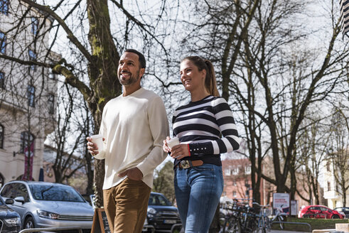 Mann und Frau mit Bechern zum Mitnehmen beim Spaziergang in der Stadt - DIGF03956
