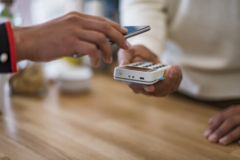 Close-up of customer paying cashless with smartphone at counter of a store - DIGF03959