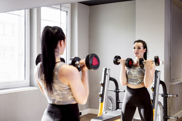 Frau hebt Hanteln im Fitnessstudio und schaut in den Spiegel - DAWF00629