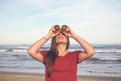 Woman using binoculars on the beach stock photo